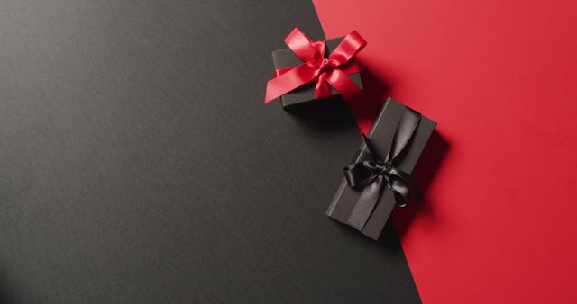 Overhead view of two black gift boxes with red and black ribbons on black and red with copy space. Luxury treat, present, shopping, black friday sale and retail concept digitally generated image.