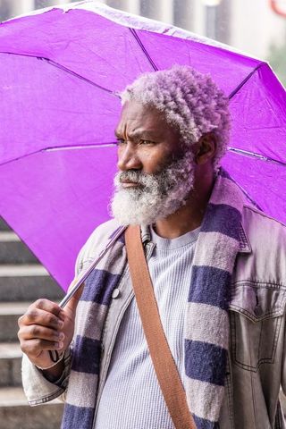 Mature african american man holding purple umbrella on rainy city steps, pensive portrait