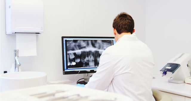 Dentist in a white coat reviewing dental x-rays on a computer screen in a modern clinic. Suitable for use in healthcare, dentistry, technology, and medical professional settings. Ideal for illustrating dental diagnostics, professional healthcare environment, and patient-care scenarios.