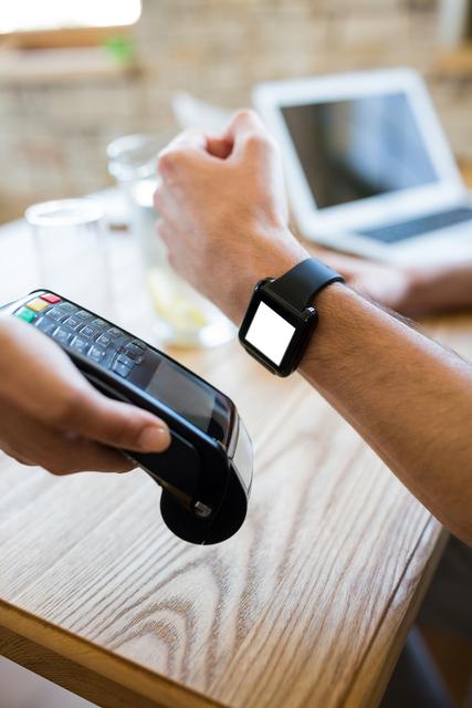 Person making contactless payment using smartwatch at a cafe. Ideal for illustrating modern payment methods, fintech, wearable technology, and convenience in everyday transactions.