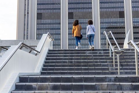 Two women walking up wide staircase toward modern office tower urban plaza