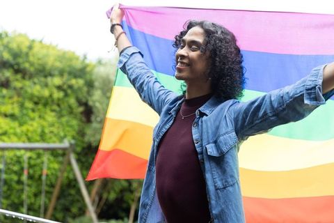 Nonbinary person celebrating with rainbow pride flag in backyard garden