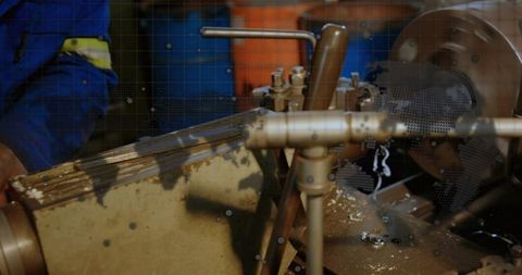 Industrial lathe turning metal with machinist in blue coverall cutting precision workpiece