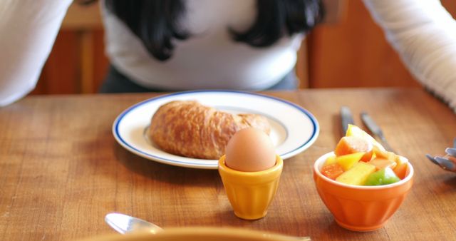 Balanced nutritious breakfast spread on table with fresh fruit bowl, boiled egg in egg cup, and croissant on plate. Ideal for illustrating healthy food habits, morning routines, nutritious diet, and breakfast ideas.