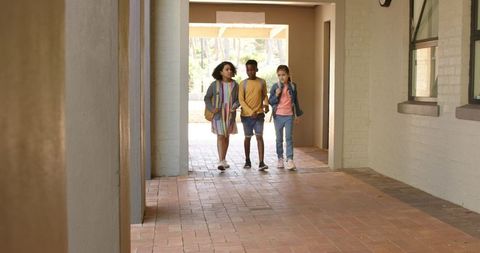 Diverse teen students walking through sunlit campus breezeway carrying backpacks