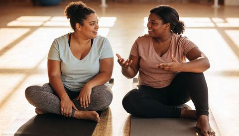 Two friends chatting on yoga mats in sunlit studio after workout