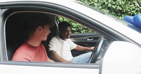 Young black driver and white friend chatting in parked white car with blue bow