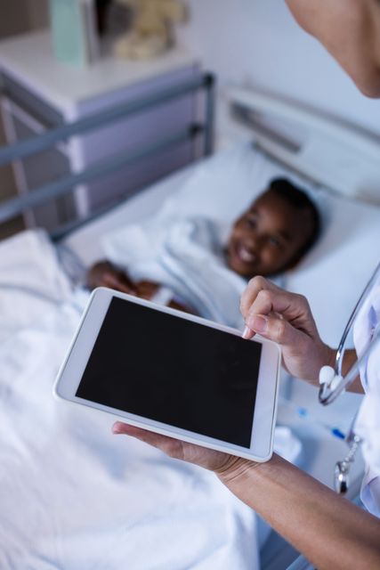 Female doctor using digital tablet while visiting a child patient in a hospital ward. Ideal for illustrating modern healthcare practices, technology in medicine, pediatric care, and patient-doctor interactions.