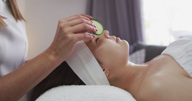 Caucasian woman lying back while beautician gives her a facial. putting cucumber slices on her eyes. customer enjoying treatment at a beauty salon.