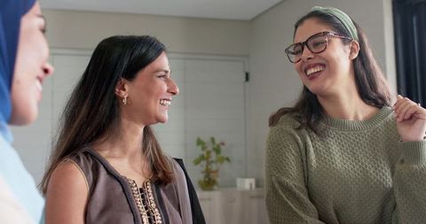 Women laughing and chatting in cozy home lounge, casual friendship and warm conversation