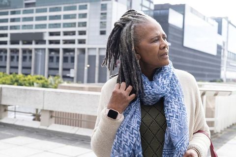 Senior african american woman touching grey dreadlocks on urban terrace wearing smartwatch