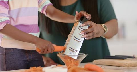 African american mother and child grating carrots together in bright home kitchen bonding