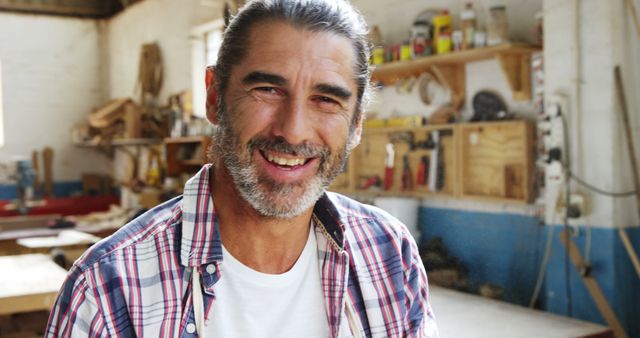 Portrait of happy mature caucasian male carpenter with beard smiling in workshop, copy space. Carpentry, woodwork, small business, construction and craft, unaltered.