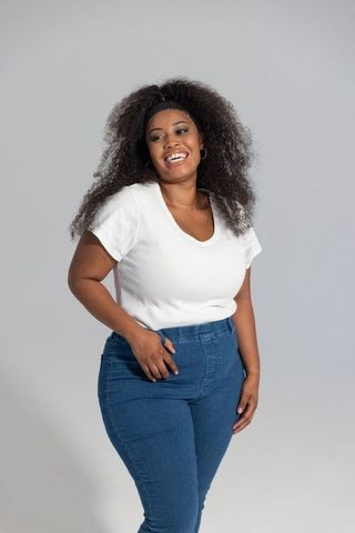 Smiling african american woman posing in white ribbed top and high-waist denim, curly hair