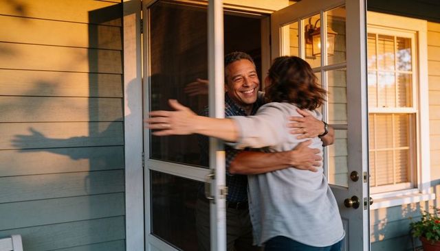 Middle-aged couple embracing on sunlit front porch during golden hour reunion