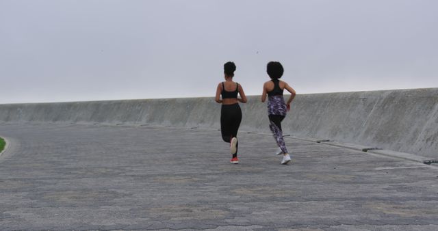 Two Women Running on Coastal Pathway on Cloudy Morning - Download Free Stock Images Pikwizard.com