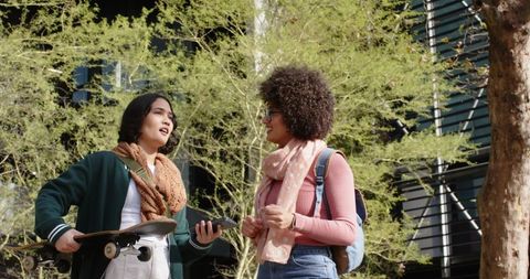College friends chatting on campus with skateboard and smartphone, casual student life