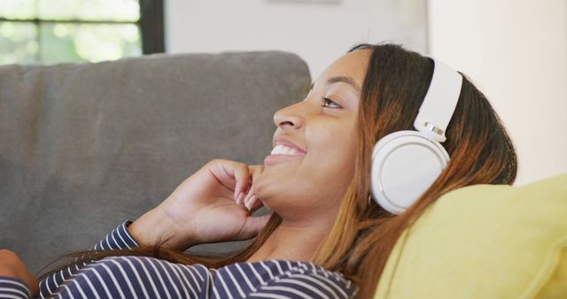 Biracial teenager girl lying on sofa and using headphones. Spending quality time, lifestyle and adolescence concept.