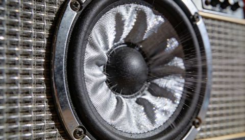 Macro closeup showing metallic woven speaker cone in amp with dust strands, chrome grille
