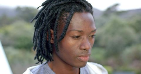 Contemplative African American Man with Dreadlocks Looking Down Outdoor Headshot with Bokeh