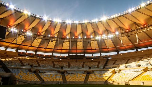 Empty modern stadium bowl at sunset with illuminated roof canopy and tiered seats