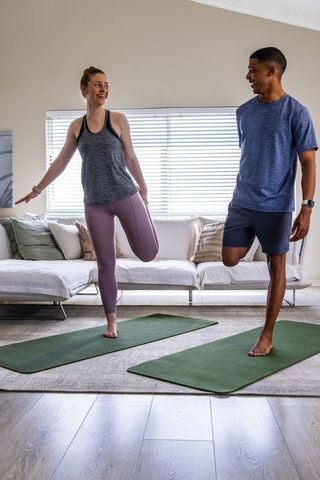 Diverse couple doing home workout quad stretch on mats in activewear with fitness trackers