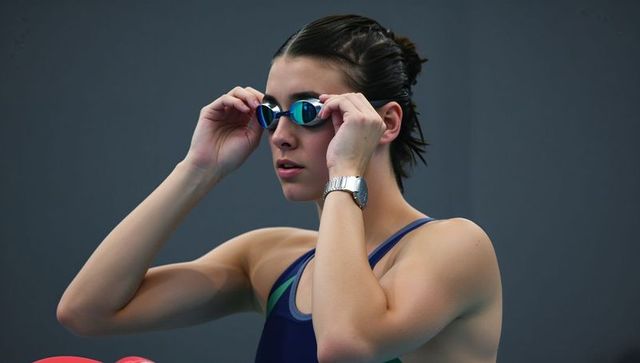 Adjusting mirrored goggles competitive swimmer wearing one-piece swimwear preparing