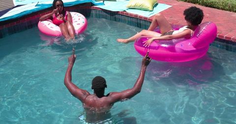 Summer friends relaxing on pink donut and inflatable lounge floats in backyard pool