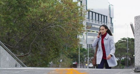 Asian woman walking up urban steps talking on smartphone, modern professional lifestyle