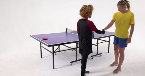 Diverse female athletes shaking hands over ping pong table in studio