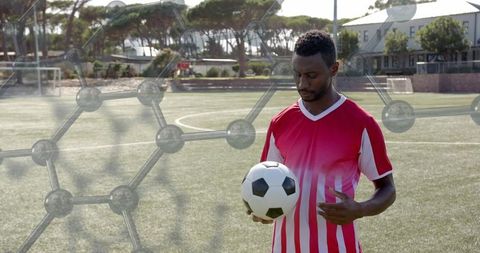 Cradling soccer ball on sunlit turf, focusing on technique, hexagonal overlay, copy space