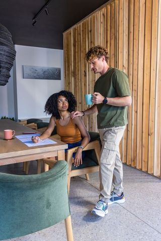 Diverse couple collaborating at cozy wooden dining nook, woman reviewing papers with pen