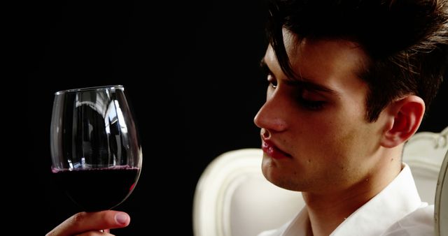 A young Caucasian man examines a glass of red wine carefully, with copy space. His focused expression suggests he might be a sommelier or a wine enthusiast appreciating the beverage's qualities.