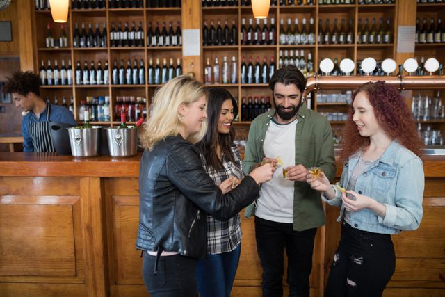 Group of friends enjoying tequila shots at a bar counter. They are smiling and socializing, creating a lively and fun atmosphere. Ideal for use in advertisements for bars, nightlife promotions, social events, and alcohol brands.
