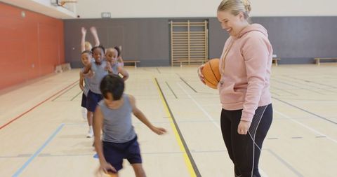 Female Coach Teaching Children Basketball Drills in School Gym