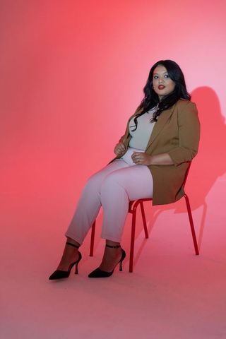 Confident plus-size professional woman sitting on red chair against pink gradient