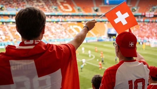 Waving swiss flag: passionate fans cheering in stadium wearing red jerseys