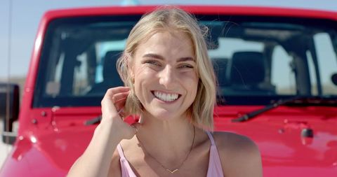 Happy Blonde Woman Smiling in Front of Red Convertible on Road Trip
