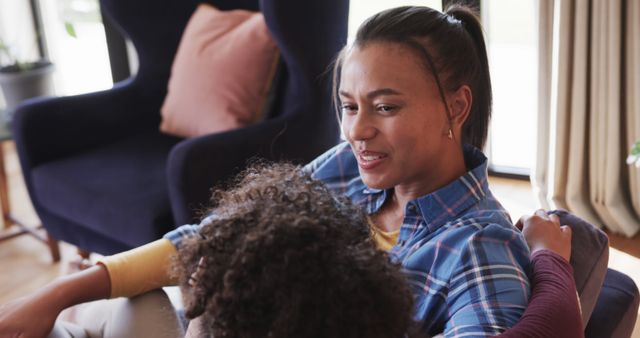 Mother and child are sitting together on a couch in a comfortable, homey environment. Mother is attentively listening while the child is leaning against her. Could be used for marketing materials related to family life, parenting blogs, or advertisements for home products and family services.