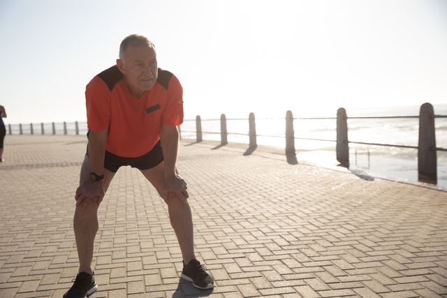 Senior Caucasian man working out on promenade by the sea wearing sports clothes, resting during workout. Retirement healthy lifestyle activity.