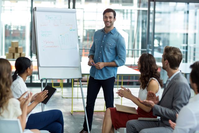 Male professional presenting ideas on whiteboard to attentive colleagues during business meeting in modern office. Ideal for illustrations of corporate workshops, team strategy sessions, leadership training, and collaborative projects.