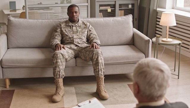 Soldier sitting on couch receiving mental health counseling with clinician holding clipboard