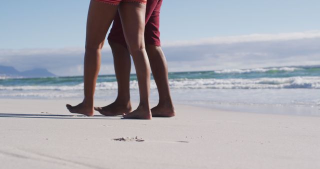 Low section of african american couple embracing and walking on the beach. healthy outdoor leisure time by the sea.