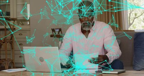 Man reviewing documents on laptop at home with cyan digital network overlay