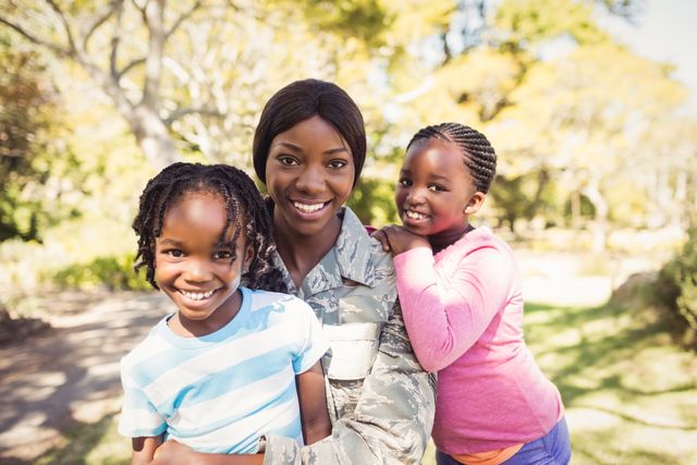 African American military mother enjoying time with her two children in a park. They are smiling and bonding, showcasing a strong family connection. Ideal for use in articles or advertisements about military families, parenting, family support, and outdoor activities.