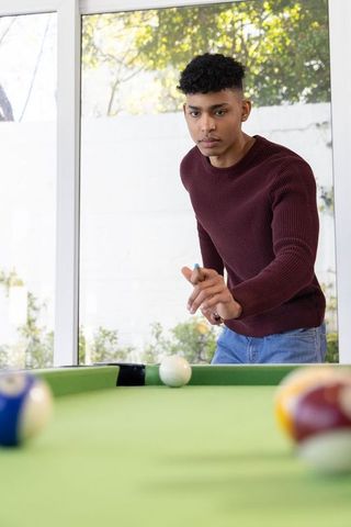 Young african american man concentrating on cue shot playing pool in sunlit home recreation room