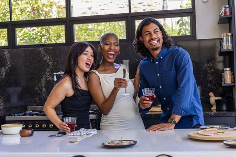 Diverse friends laughing and clinking glasses at modern kitchen island during celebration