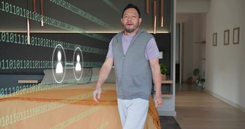 Asian man walking in contemporary bedroom with augmented reality binary data stream and ui