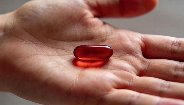 Closeup hand holding red translucent softgel capsule in palm wellness medicine concept