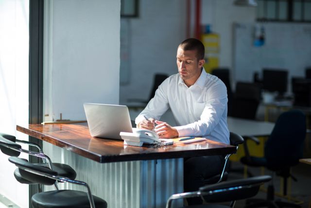 Businessman in white shirt working on laptop at modern office desk. Ideal for business, productivity, work environment, and office-related concepts.